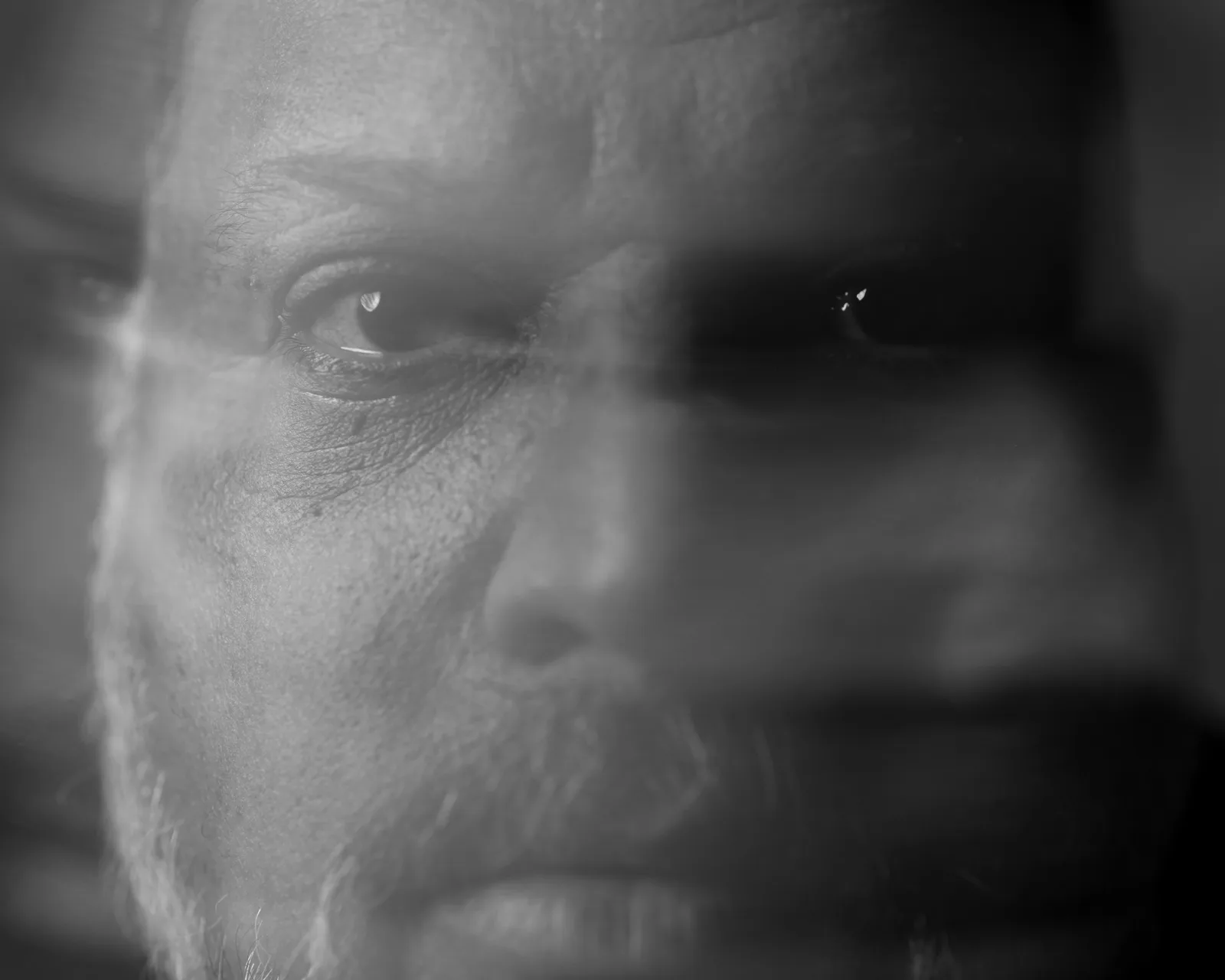 Extreme black-and-white close-up of a man's eyes, intense gaze, skin texture and faint scar visible, dramatic shadow across right side.
