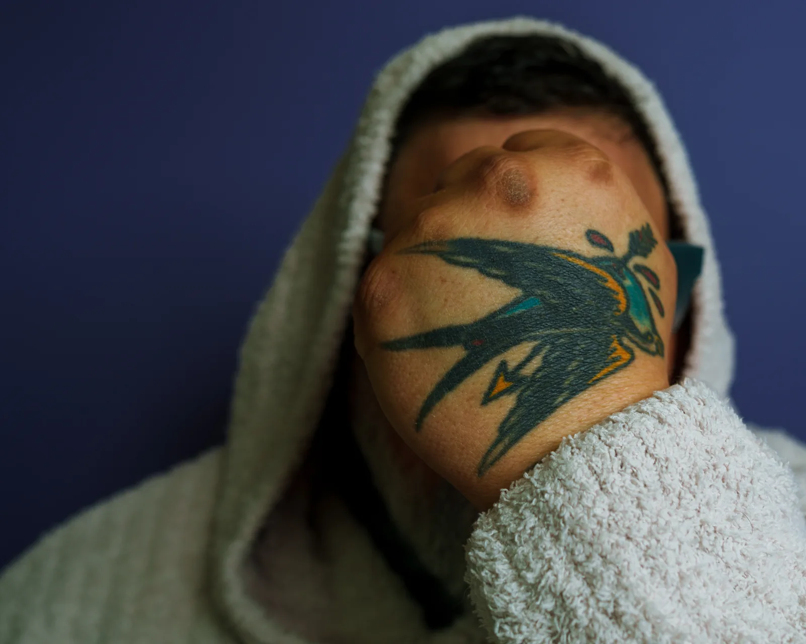 Close-up of a man's shoulder showing a large colorful swallow tattoo, his head wrapped in a pale terrycloth towel.