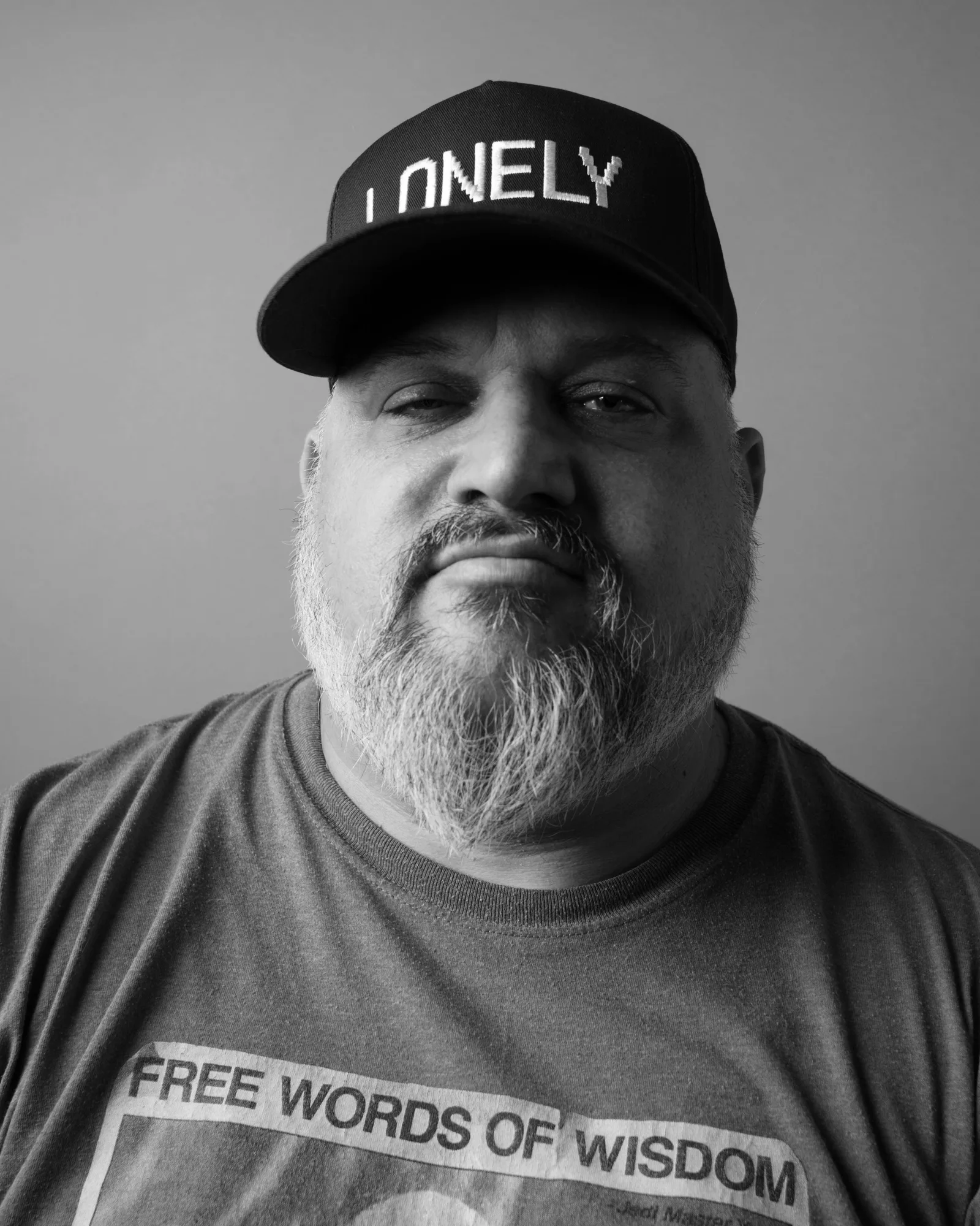 Black-and-white tight crop of a bearded man's face under a cap, mouth set firm, eyes steady and tired.