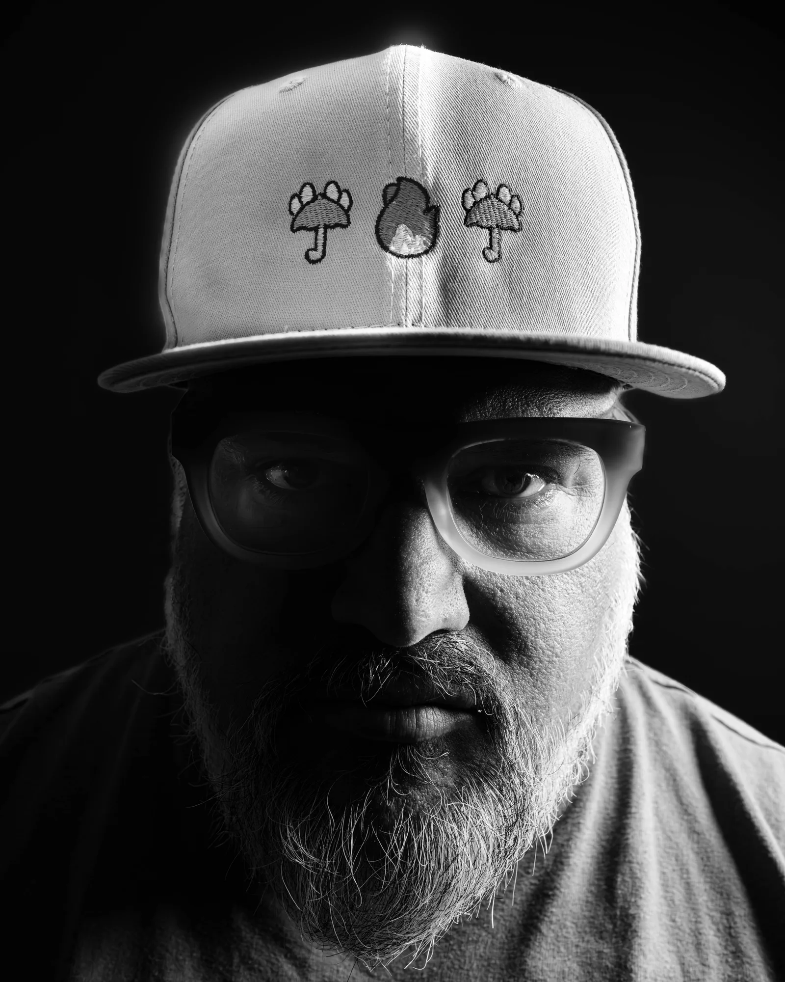 Black-and-white tight crop on a bearded man's mouth and chin, lips closed, gray-streaked beard catching light against a dark background.